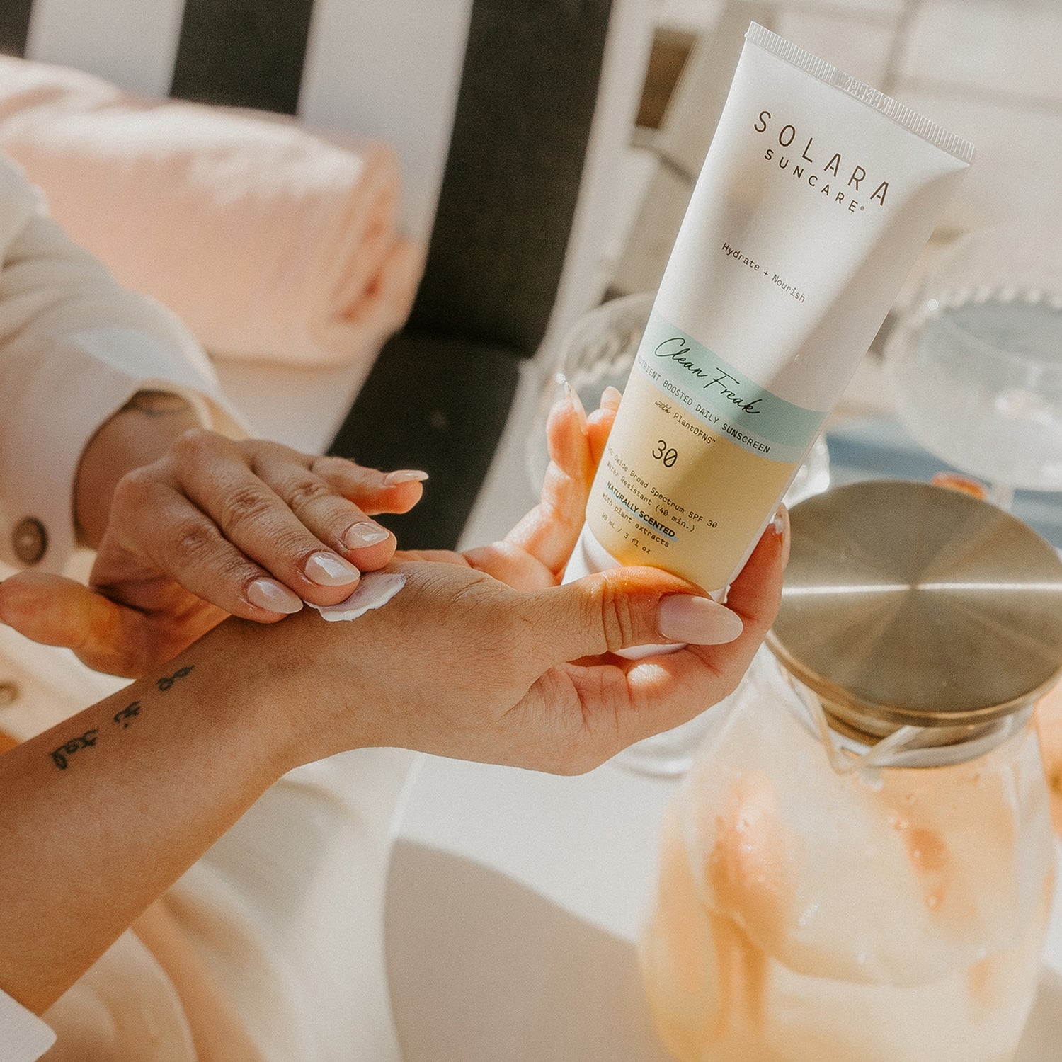 Woman applying Clean Freak mineral SPF 30 body moisturizer to arms outdoors